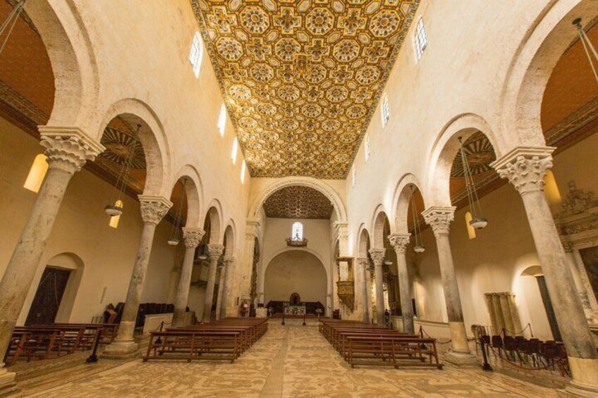 An interior with a patterned ceiling, arches, and rows of benches. 3