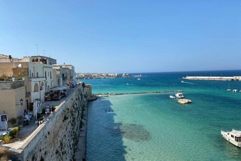 A coastal town with buildings along the waterfront, clear turquoise sea, and boats anchored near the shore. 5