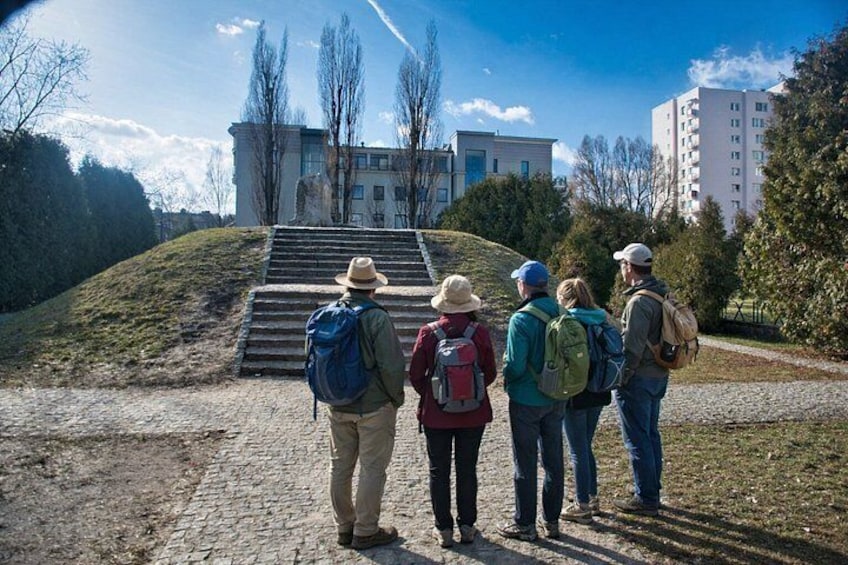 A group of people standing on a path, looking at a building with steps leading up to it. 1