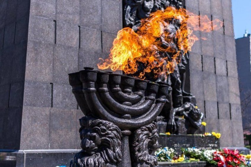 A menorah with flames, a lion sculpture, and a building in the background. 1