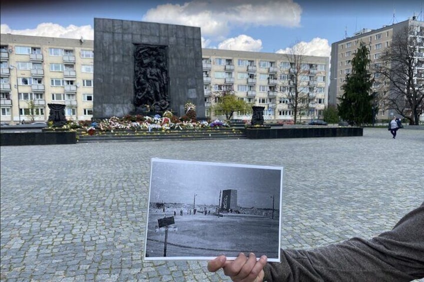 A person holding a photograph of a building, with a monument and apartment buildings in the background. 5