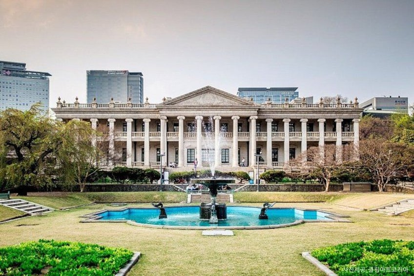 A classical building with columns, a fountain, and a well-maintained lawn. 1