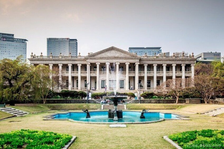 A classical building with a central fountain, surrounded by a well-maintained lawn and trees. 1