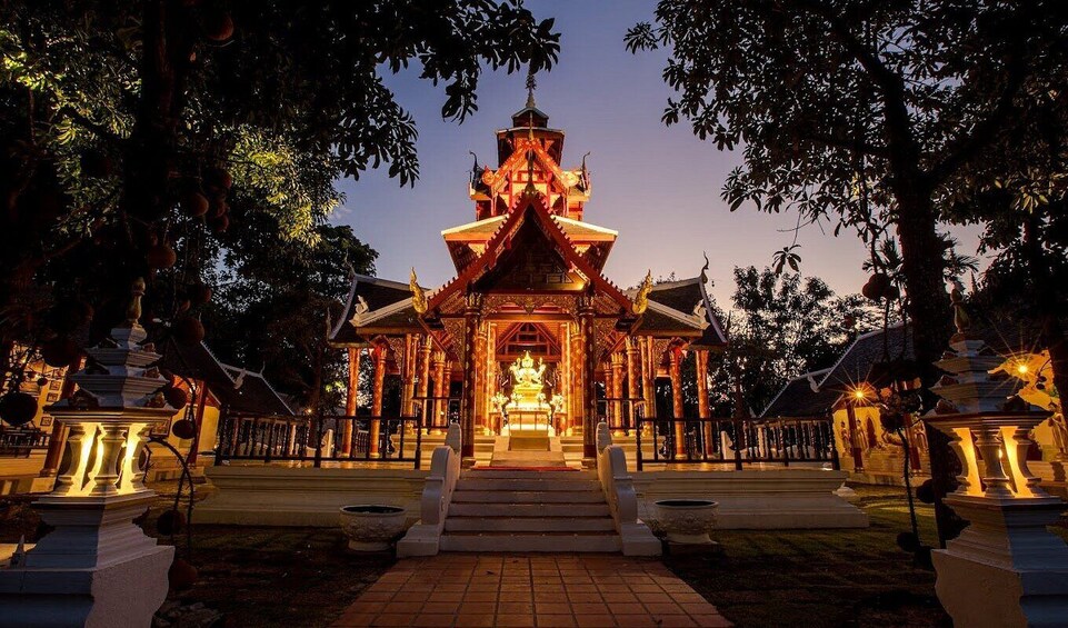 Een tempel met een centraal gouden beeld, omgeven door bomen en verlicht met warm licht. 1