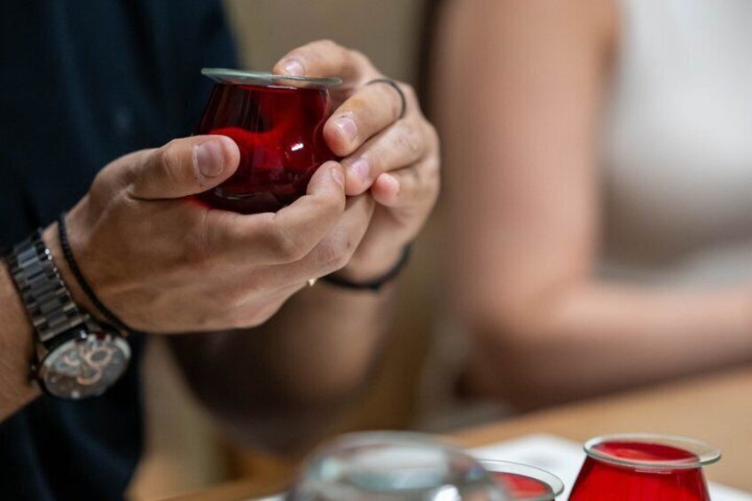 A person holding a red cup, possibly containing tea, with a watch on their wrist. 2