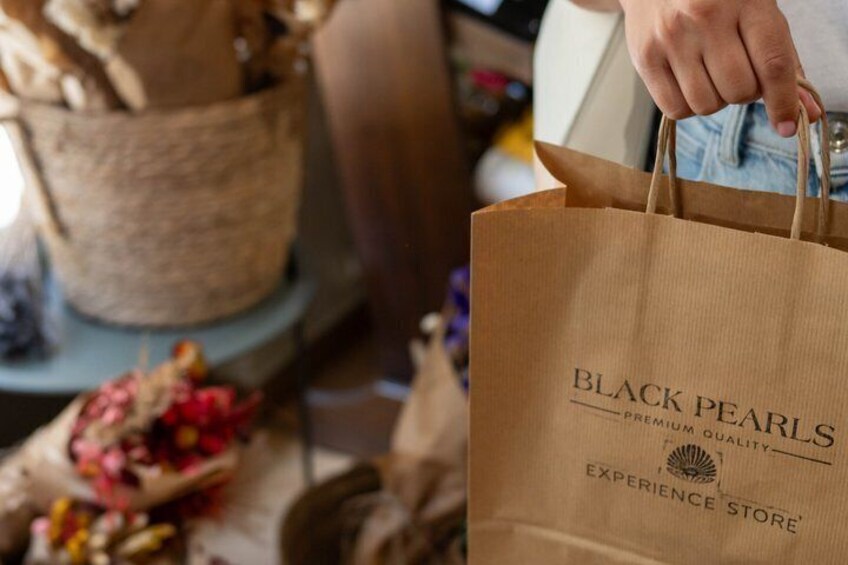 A person holding a brown paper bag with 'BLACK PEARLS PREMIUM QUALITY EXPERIENCE STORE' printed on it. 4