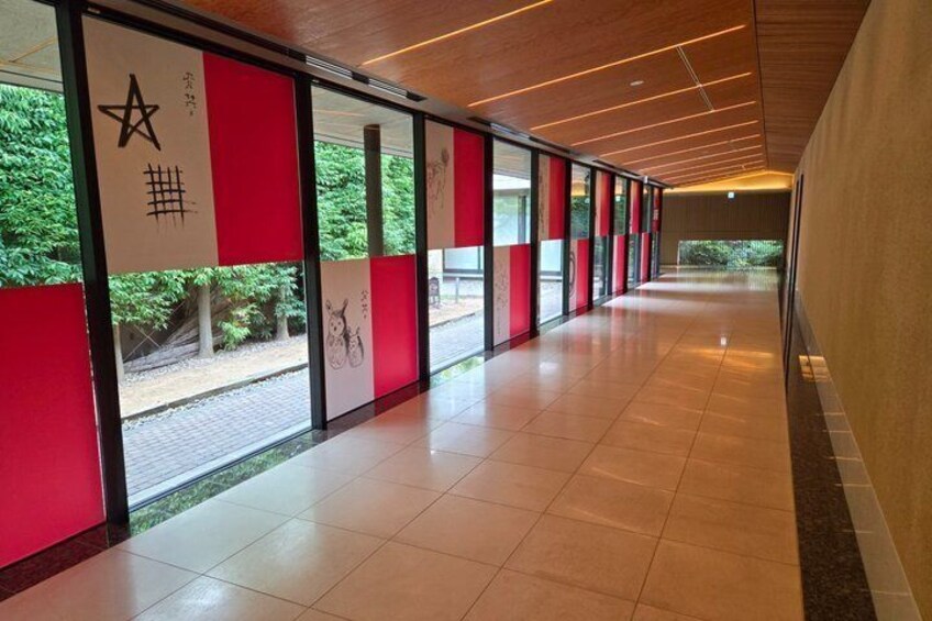 A corridor with red panels, a tiled floor, and a view of greenery outside. 2