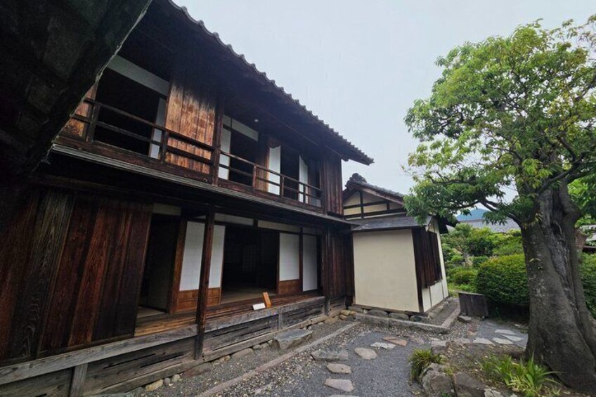 A traditional wooden house with a balcony, surrounded by a stone pathway and greenery. 4