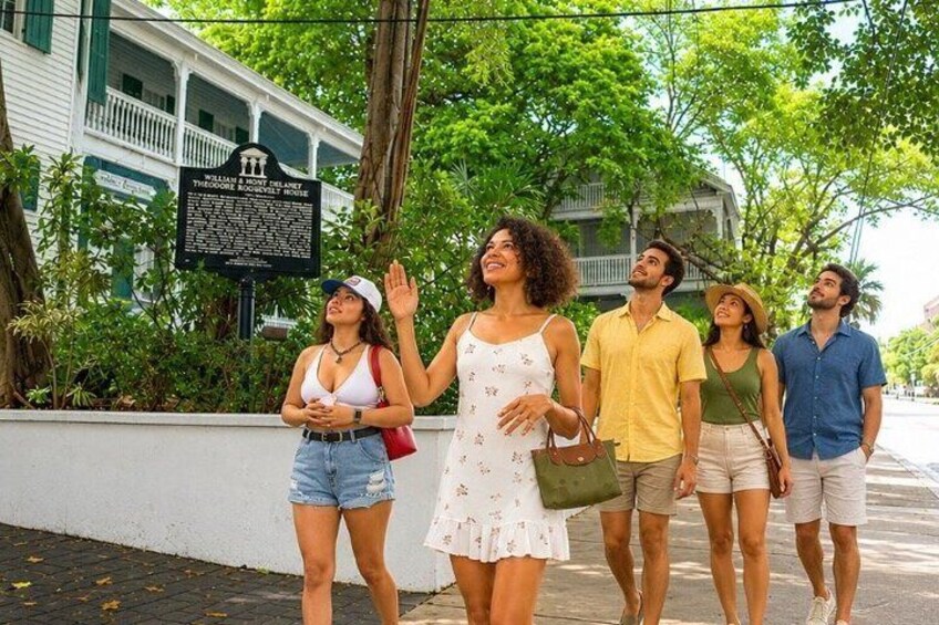 A group of people walking on a sidewalk with a historical marker in the background. 2
