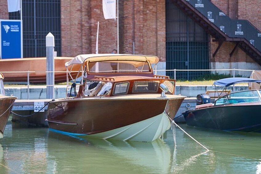 A wooden boat docked at a marina with a brick building in the background. 1