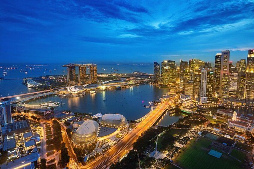 A cityscape at dusk with illuminated buildings, a prominent tower, and a large stadium. 2