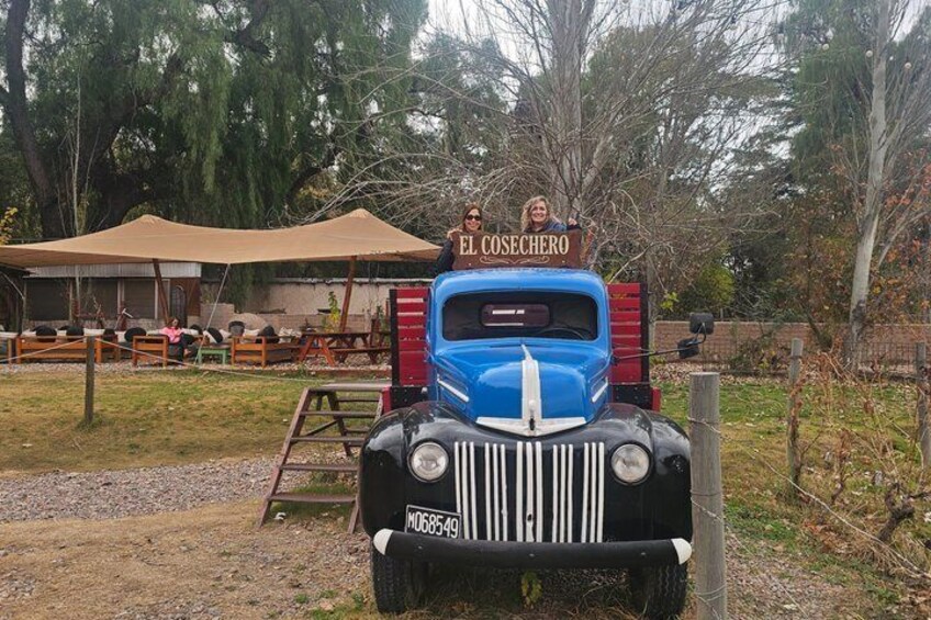 A vintage truck with 'EL COSECHERO' signage, parked in a rural setting with picnic tables and trees in the background. 1