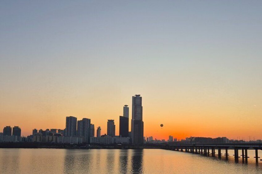A city skyline at sunset with a prominent skyscraper and a bridge over a body of water. 3