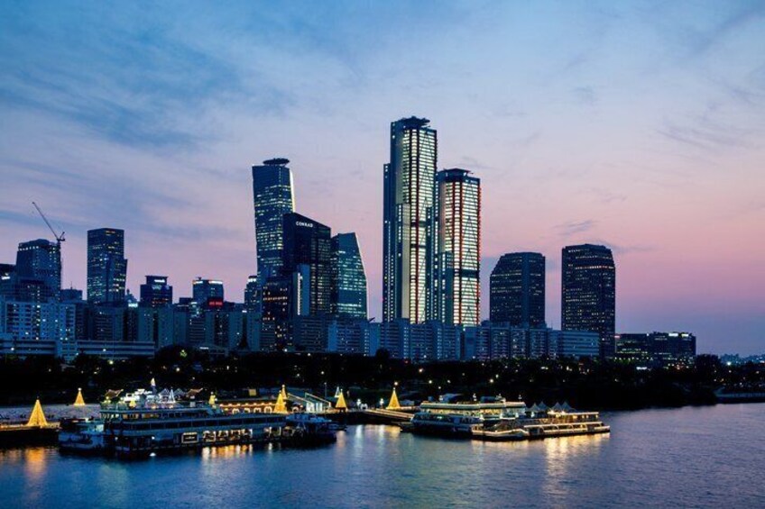 A city skyline at dusk with illuminated buildings and a river with boats. 5