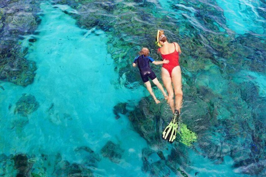 Two people snorkeling in clear blue water with visible underwater rocks. 5