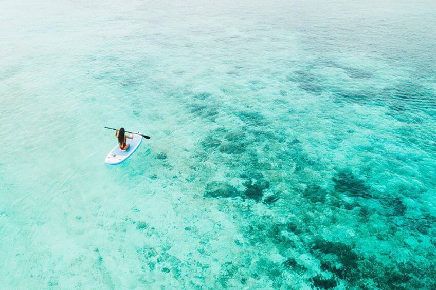 A person paddleboarding on clear turquoise water with visible coral reefs. 3