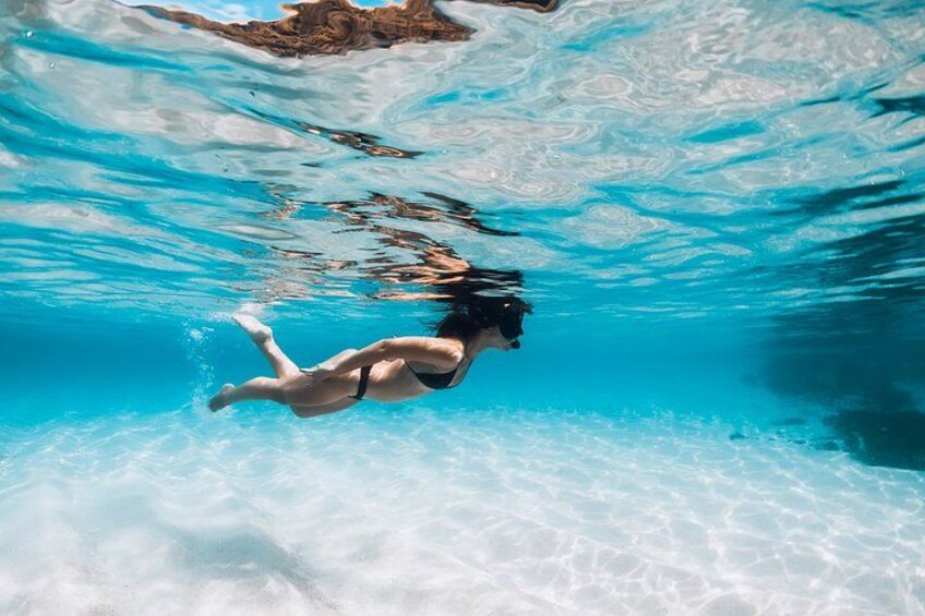 A person swimming underwater in a clear blue pool. 2