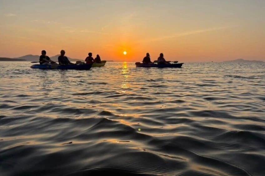 A sunset over calm water with people in small boats. 1