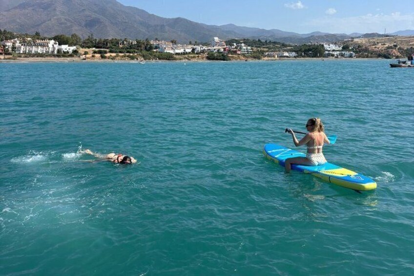 A person paddleboarding on a calm sea with a mountainous landscape in the background. 2