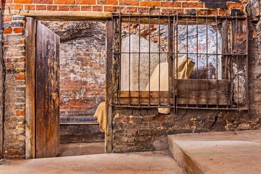 An old brick building with a barred window and a large wooden door. 4