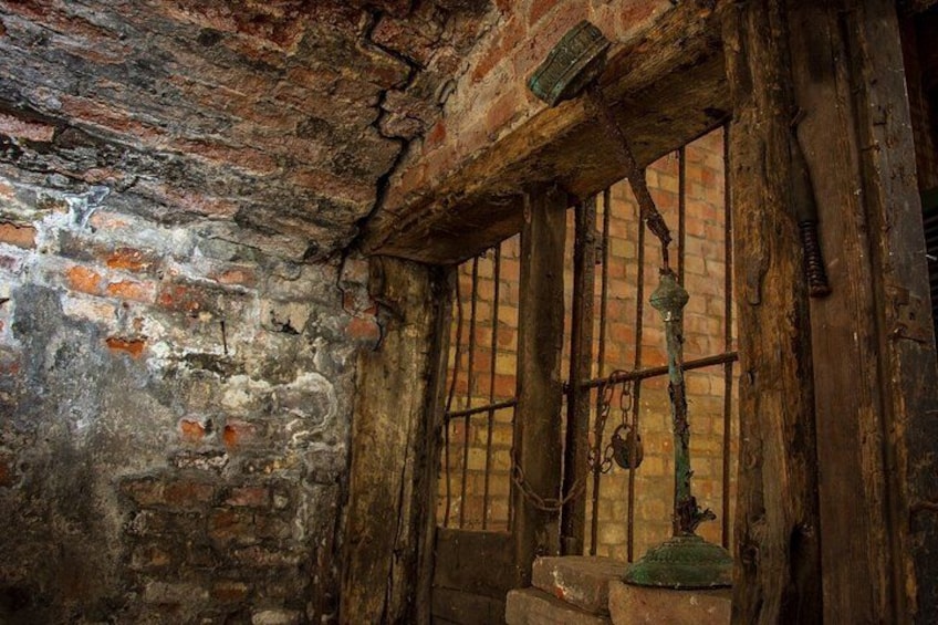 A rustic room with exposed brick walls, wooden beams, and a barred window. 2