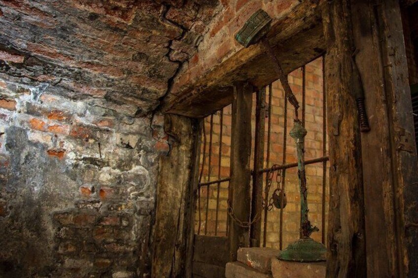 An old, rustic room with exposed brick walls, wooden beams, and a barred window. 3