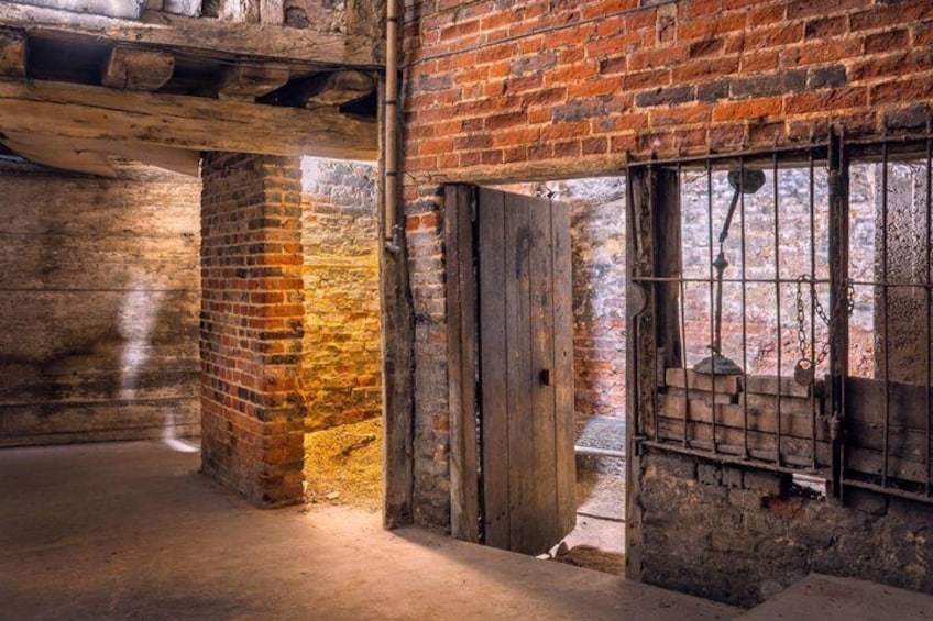 An old brick building with exposed wooden beams, a barred window, and a concrete floor. 1