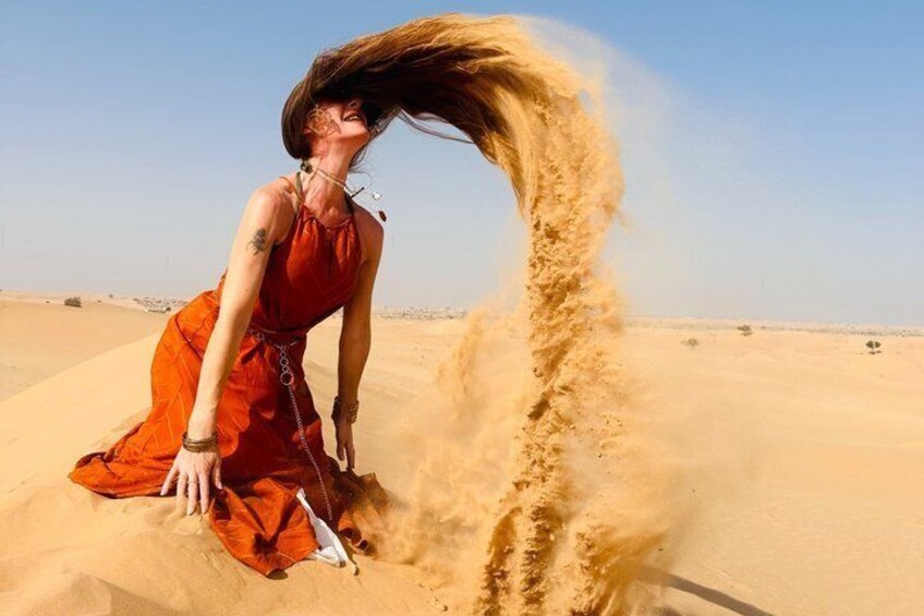 A person in an orange dress blowing sand in a desert. 1