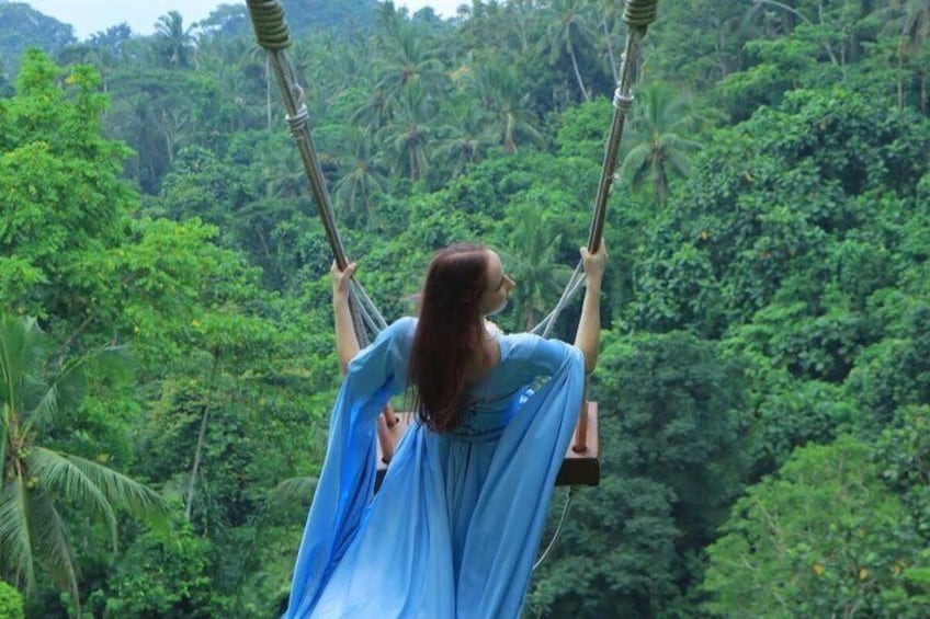 A person in a blue dress on a swing with a lush green forest background. 3