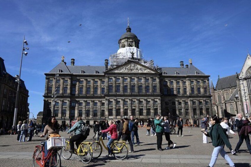 A historic building with a dome and columns, surrounded by people and bicycles. 1