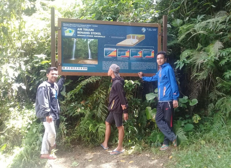 Three individuals standing in front of an informational sign about the Air Terjun Benang Stokel Waterfalls. 5