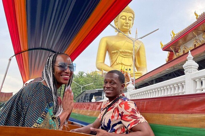 Two people in front of a large golden Buddha statue with a colorful backdrop. 3