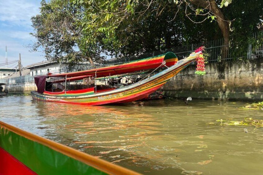 A colorful boat with a green canopy, docked near a tree-lined canal. 4