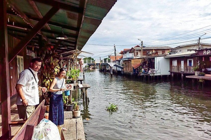 A river with houses on stilts, a man and woman standing on a dock, and a boat in the background. 5