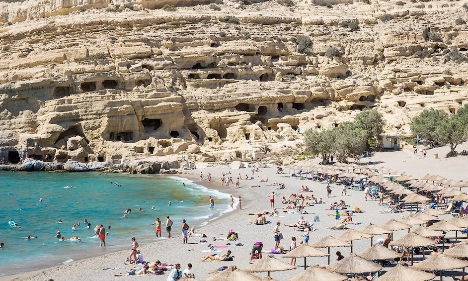 A beach with people sunbathing and swimming, surrounded by rocky cliffs with caves. 5