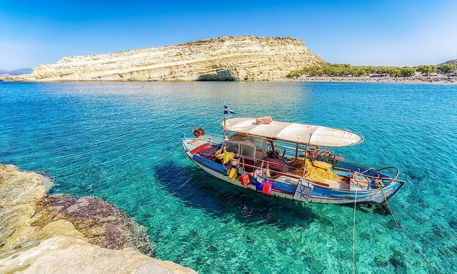 A boat anchored in clear turquoise waters with a rocky coastline and a hill in the background. 3