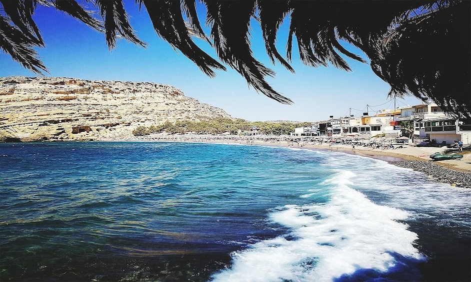 A coastal town with a beach, clear blue sea, rocky cliffs, and buildings along the shore. 5