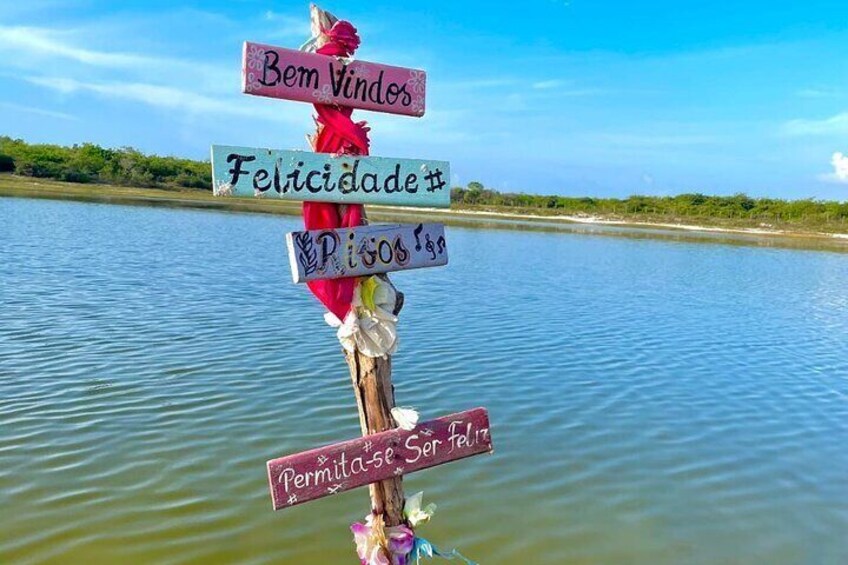 A wooden signpost with multiple signs, including 'Bem Vindos,' 'Felicidade,' and 'Pisos.' 3