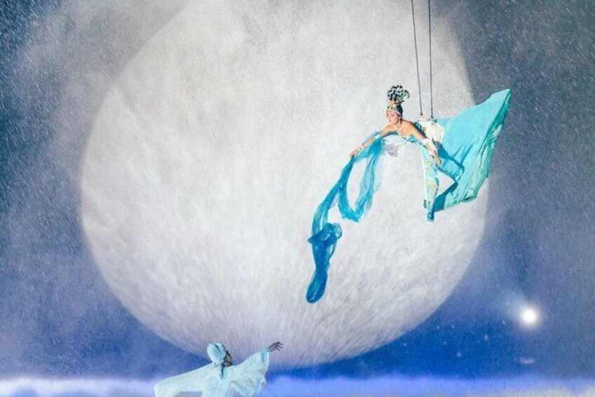 A person in a flowing blue dress suspended by ropes against a backdrop of a large moon. 2