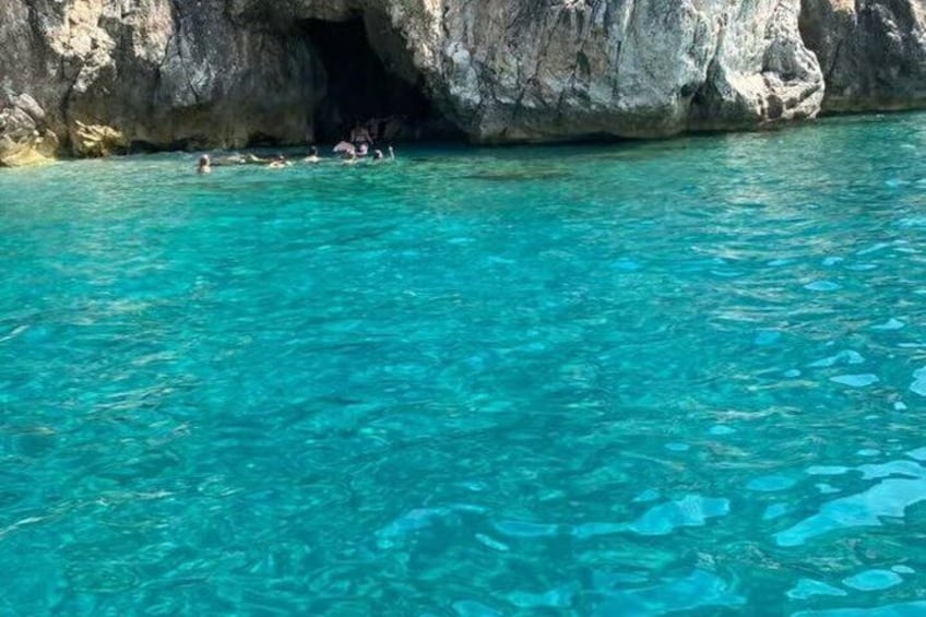 Clear turquoise water, a rocky cave entrance, and people swimming. 5