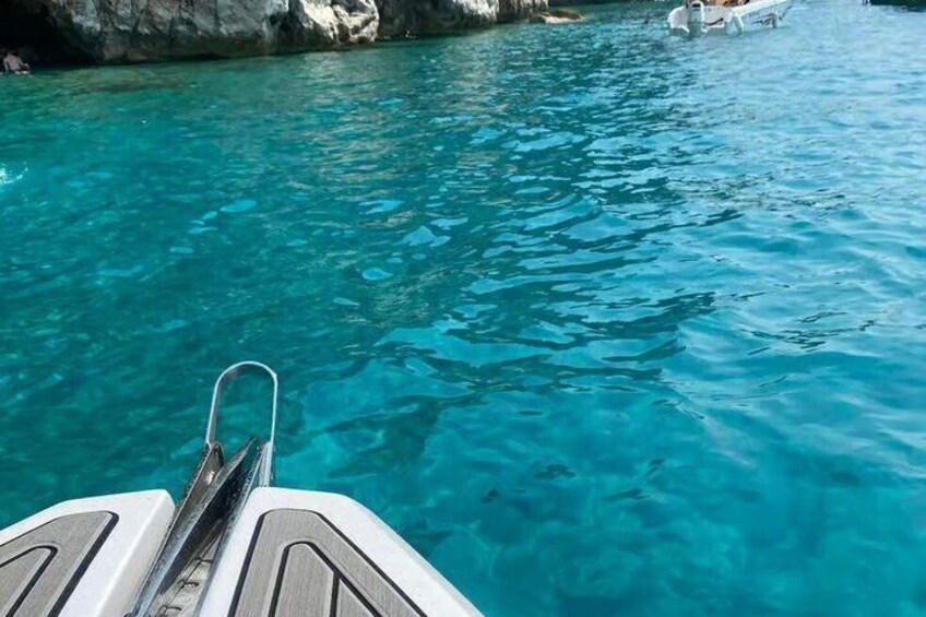 A boat's wake in clear turquoise water, rocky shoreline, and a distant person on a boat. 3