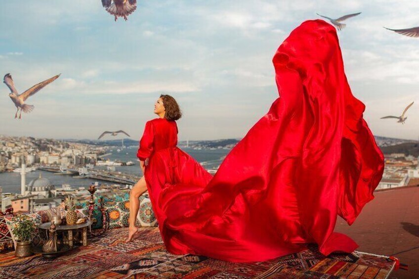 A person in a red dress sitting on a patterned rug with a cityscape and birds in the background. 1