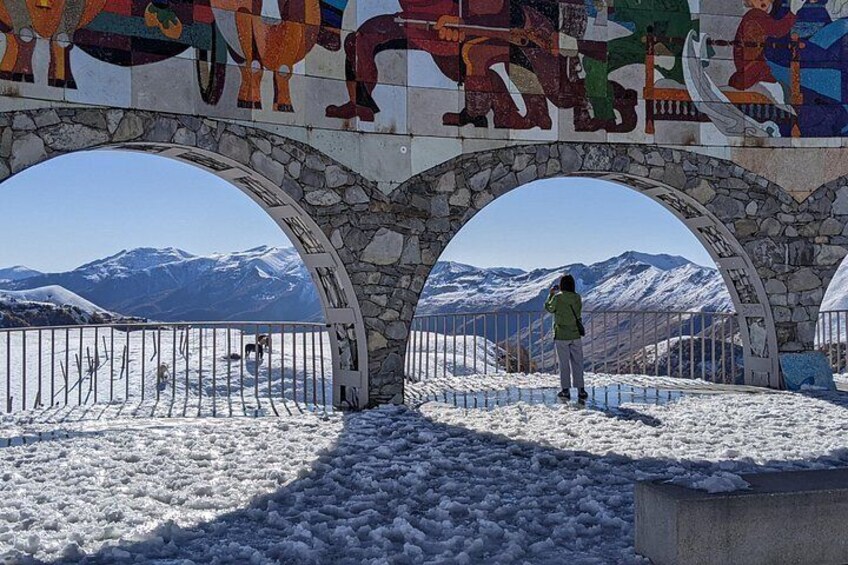 A stone bridge with colorful murals, snow-covered ground, and a mountainous landscape in the background. 3