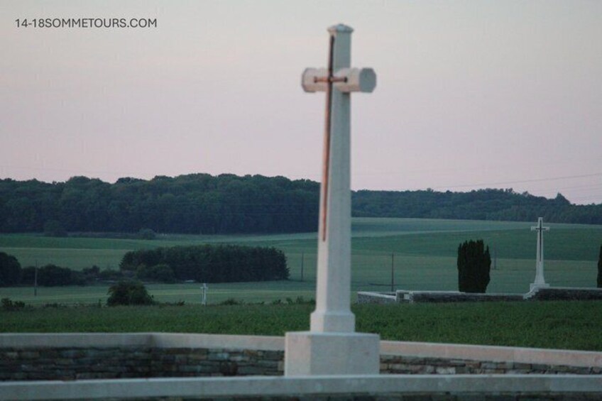 A white cross monument in a rural setting with a green field and trees in the background. 5