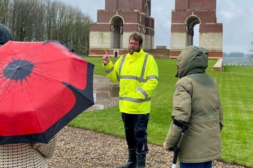 A person in a yellow jacket standing on a grassy field with a red umbrella, a historic building in the background, and a clear sky. 2