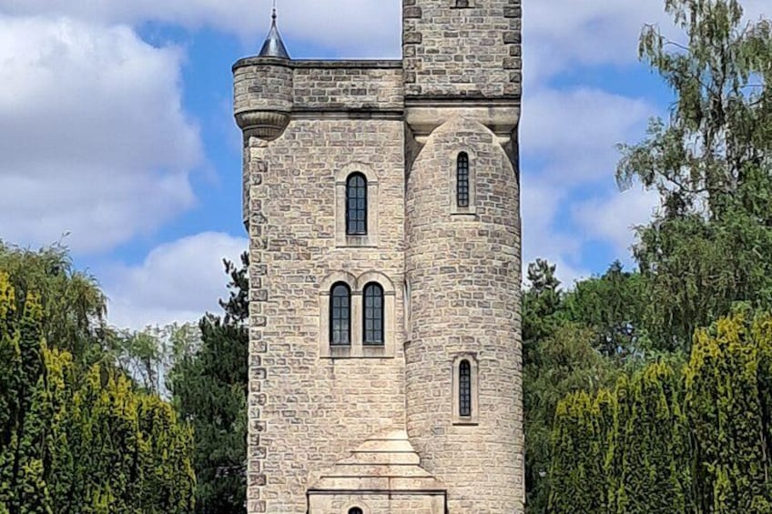 A stone tower with arched windows and a turret, surrounded by trees. 3