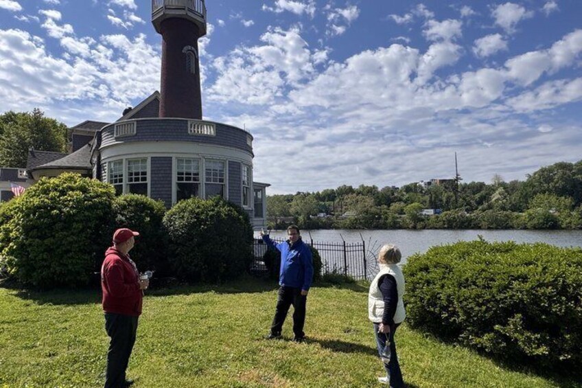 A lighthouse, a lake, and people standing on grass. 2