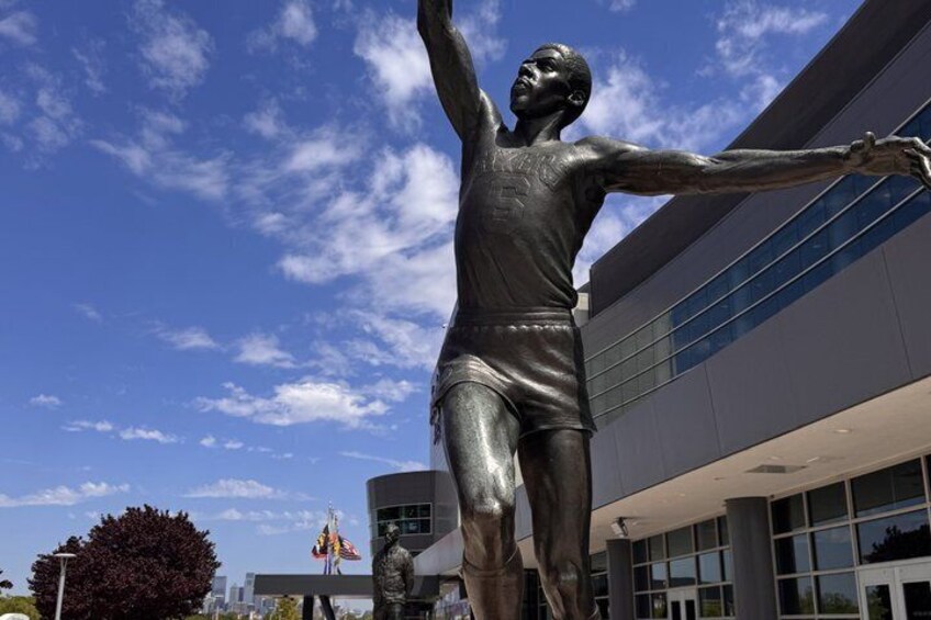 A statue of a basketball player with arms raised, a building with glass windows, and a clear blue sky. 4