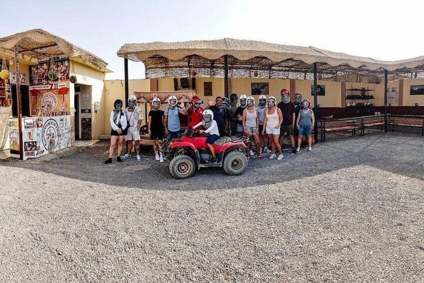 A group of people standing around a red ATV in a gravel area with a building in the background. 5