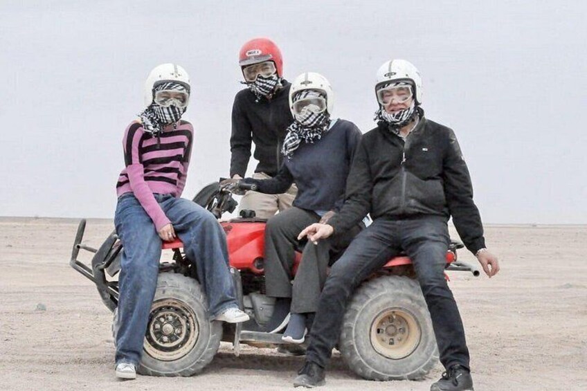 Four people on a red ATV in a barren landscape. 2
